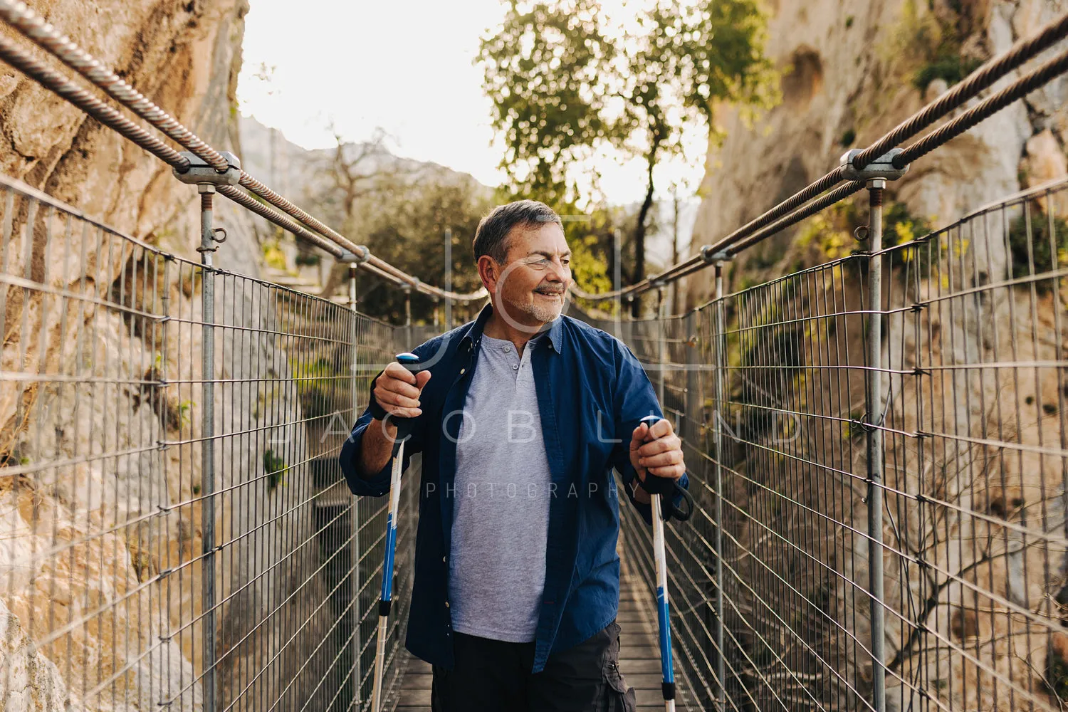 Adventurous senior man crossing a bridge with hiking poles
