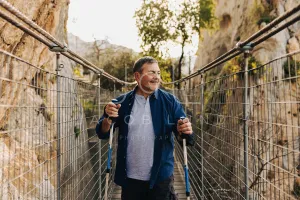 Adventurous senior man crossing a bridge with hiking poles